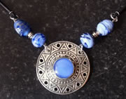 Necklace: blue beads, circular silver setting with geometrical patterns, glue glass circle at centre