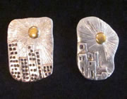 Two silver pendants: sun shining over tall middle-eastern buildings